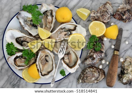 Oysters on crushed ice with antique oyster knife and silver fork with lemon fruit and pearls on a tin plate on a marble slab.