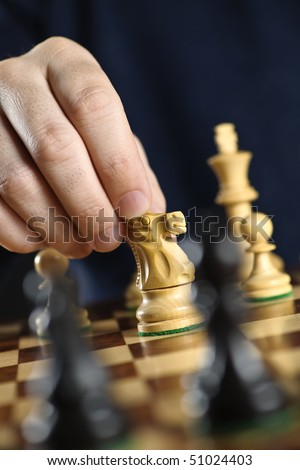 Hand moving a knight chess piece on wooden chessboard