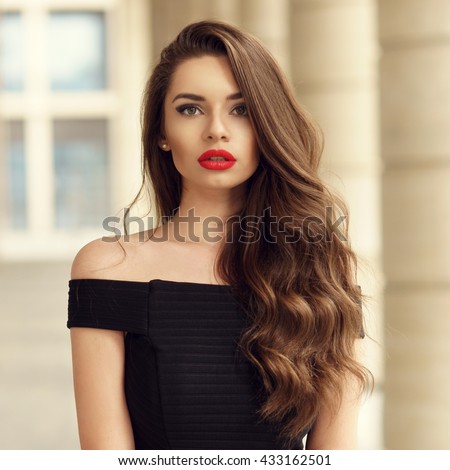 Đóng lên bức chân dung của người phụ nữ trẻ xinh đẹp với tóc nâu dài xoăn tóc giả contre nền kiến trúc và nhìn bạn