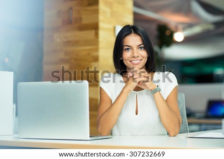 Portrait of a cheerful businesswoman sitting at the table in office and looking at camera
