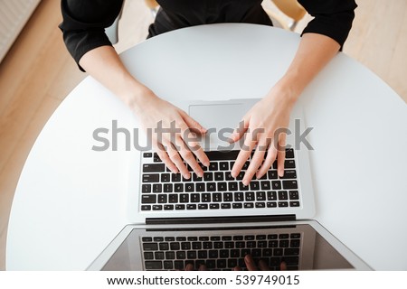 Top view photo of young lady worker sitting in office while using laptop computer and typing by keyboard.