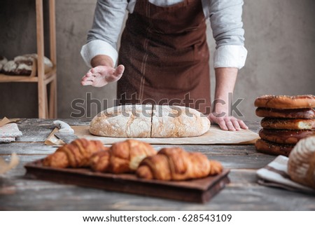 Cropped image of young man baker cut the bread.
