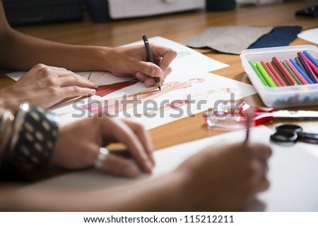 two young women working as fashion designers and drawing sketches for clothes in atelier. Cropped view