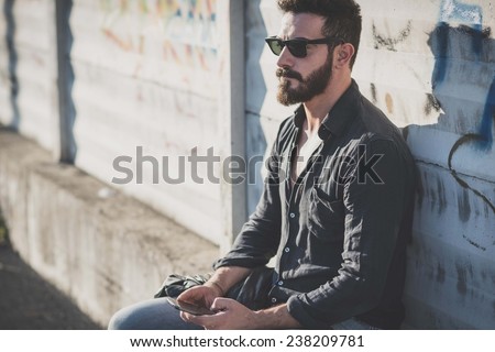 young handsome attractive bearded model man using smartphone in urban context