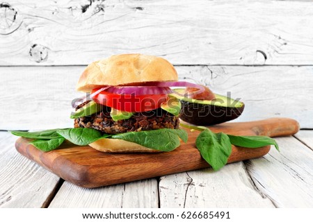 Vegetarian bean and sweet potato burger with avocado and spinach against a rustic white wood background