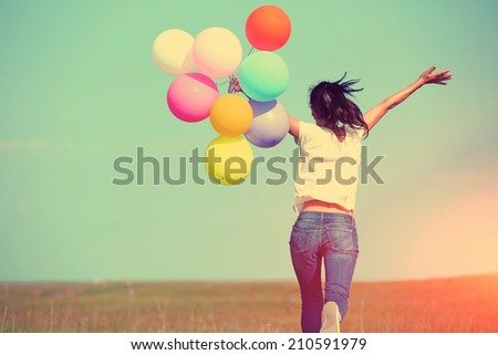 young asian woman running and jumping on green grassland with colored balloons
