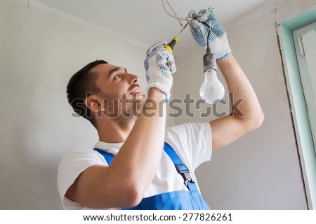 building, renovation, technology, electricity and people concept - builder with screwdriver fixing socket indoors