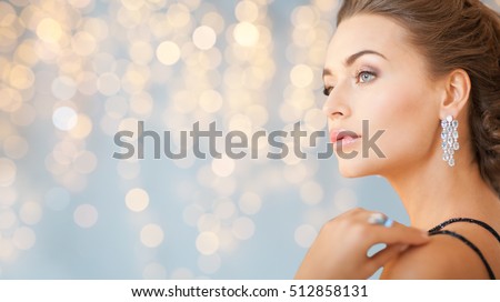 people, holidays, jewelry and luxury concept - close up of woman in evening dress with diamond earring over lights background