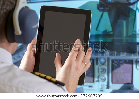 Airline pilot wearing uniform with epauletes using tablet in airplane cockpit