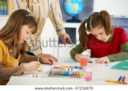 Elementary age children sitting around desk enjoying painting with colors in art class at primary school classroom.