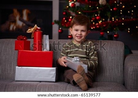 Portrait of happy little boy sitting on couch with christmas presents, smiling.?