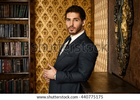 Respectable young man standing by a fireplace in a room with classic interior. Luxury. Men's beauty, fashion.
