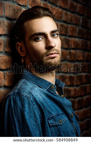 Jeans style. Portrait of a handsome young man in jeans clohes standing against the brick wall. Men's beauty, fashion. Men's barbershop, Hairstyle.