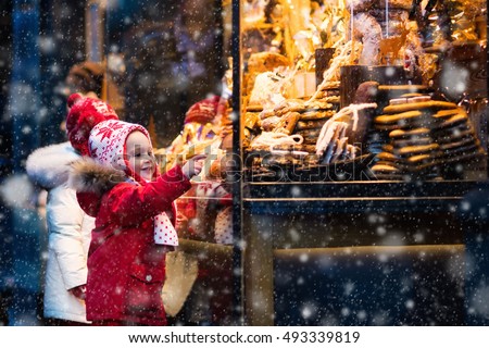 Children window shopping on traditional Christmas market in Germany on snowy winter day. Kids buying candy, pastry and gingerbread in confectionery. Boy and girl choosing sweets in Xmas bakery.
