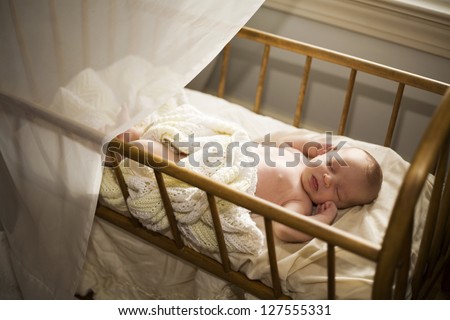 Adorable baby asleep in his cradle by a window.