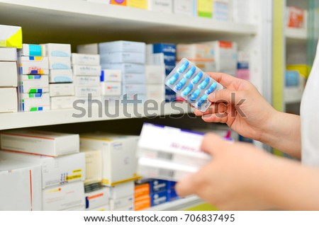 Pharmacist holding medicine box and capsule pack in pharmacy drugstore.