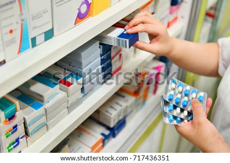 Pharmacist holding medicine box and capsule pack in pharmacy drugstore.