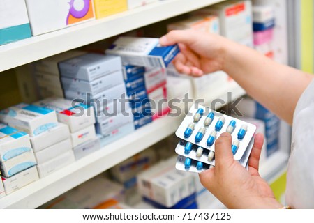 Pharmacist holding medicine box and capsule pack in pharmacy drugstore.