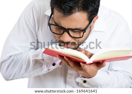 Closeup portrait of young nerdy guy with big black eye glasses trying to read book but having difficulties seeing text because of vision problems. Negative emotion facial expression feelings