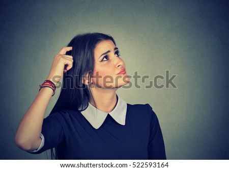 Portrait confused thinking young woman bewildered scratching her head seeks a solution looking up isolated on gray wall background. Human face expression