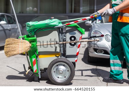 Worker of cleaning company in green uniform with garbage bin and a broom. Utility service company men worker of municipality sweeping city streets.