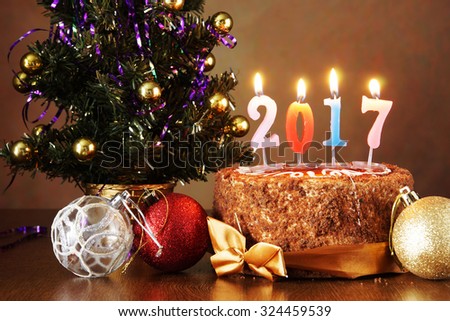 New Year 2017 still life. Chocolate cake and artificial fir tree with burning candles on brown background