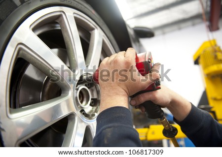 Detail image of mechanic hands with tool, changing tyre of car, with blurred background of garage.
