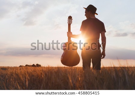 silhouette of musician with guitar at sunset field, music background