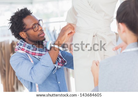 Fashion designers standing next to a model and adjusting a dress