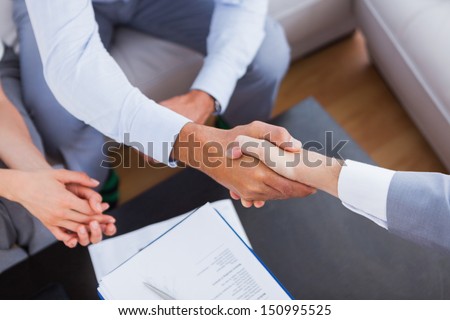 Salesman shaking hands with client with contract on the coffee table
