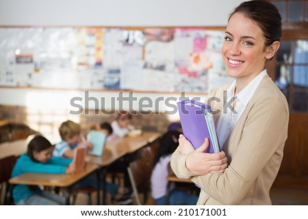 Pretty teacher smiling at camera at back of classroom at the elementary school