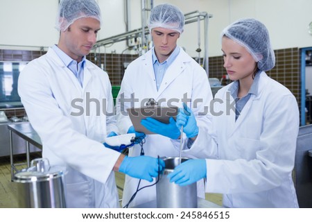 Man writing on clipboard while colleagues testing product in the factory
