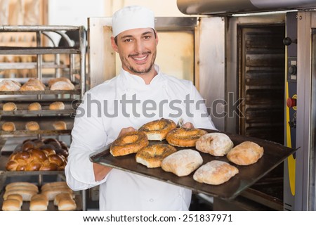 Happy baker showing tray of fresh bread in the kitchen of the bakery