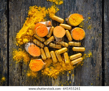 Turmeric powder and turmeric capsules on wooden background