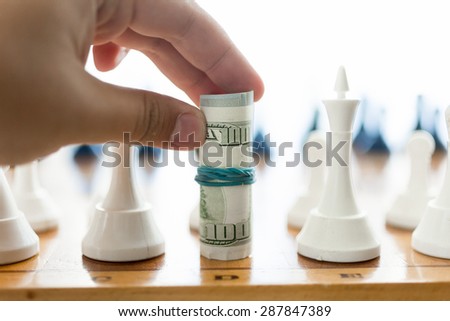 Closeup shot of male hand holding twisted banknotes and making move at chess