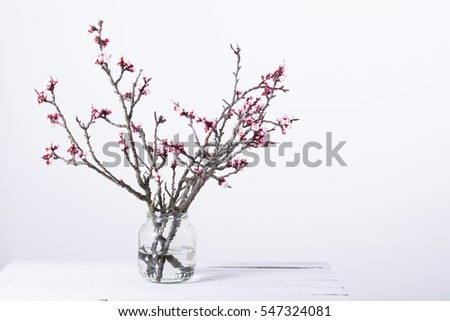 pink blossoming peach flower branches at simple old glass jar on white wooden table