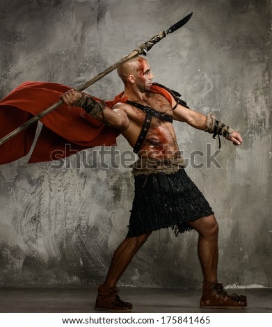 Wounded gladiator in red coat throwing spear - stock photo