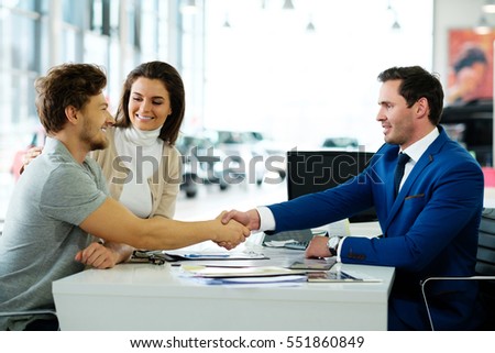 Salesman and customer shaking hands congratulating each other at the dealership showroom.