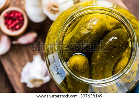 Pickled gherkins in jar, fermented food with spices, view from overhead on wooden table