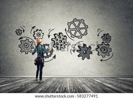 Back view of engineer woman in hardhat and sketched concept of teamwork on wall