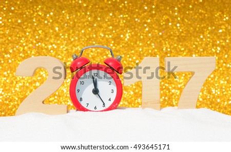 Happy new year 2017 greeting card. Alarm clock and the wooden numbers 2017 in a snowdrift on a gold glitter background