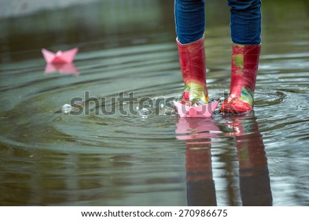 girl runs the pink paper boat in a puddle in the rain, spring