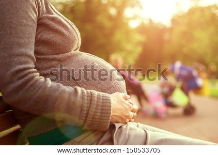 Pregnant woman sitting on a bench. on background the children play. warm weather