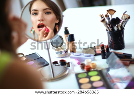 Young beautiful woman making make-up near mirror,sitting at the desk