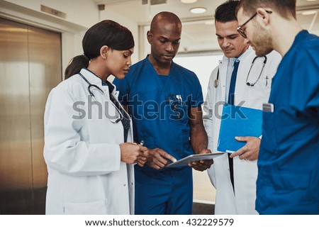 Multiracial team of doctors discussing a patient standing grouped in the foyer looking at a tablet computer, close up view