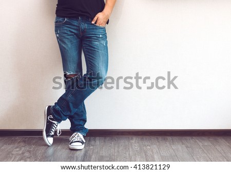 Young fashion man's legs in jeans and sneakers on wooden floor