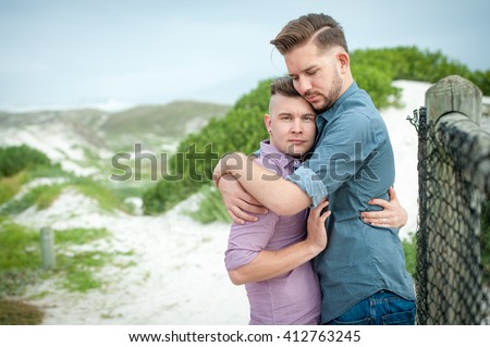 stock-photo-two-gay-men-lovingly-embrace-and-kiss-next-to-a-beach-fence-412763245.jpg