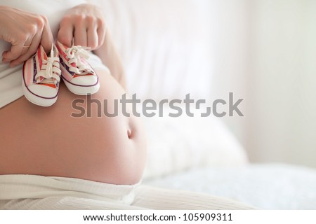 Small shoes for the unborn baby in the belly of pregnant woman