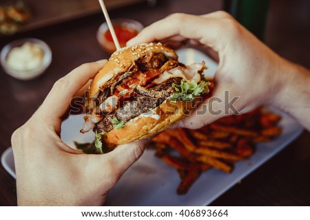 man holds burger with hands and sweet potato fries and dips on background in cafe