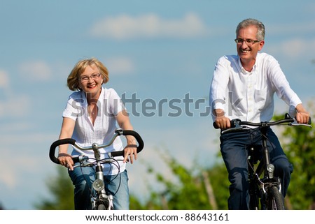 Happy mature couple - senior people (man and woman) already retired - cycling in summer in nature